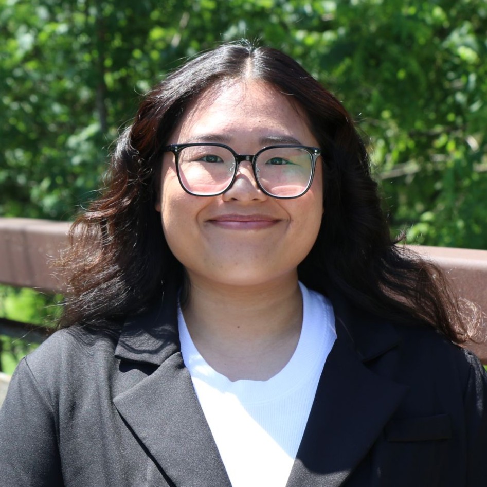 Woman with long wavy black hair wearing glasses and a black suit jacket with a white shirt