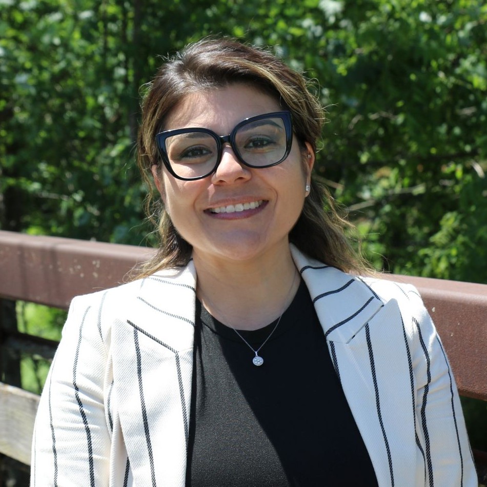 Woman with hair pulled back wearing black glasses and a white striped suit jacket and a black shirt