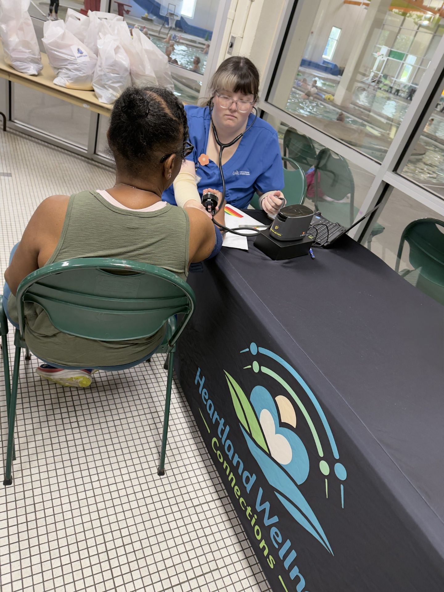 A woman is sitting in a chair facing a healthcare professional who is checking her blood pressure