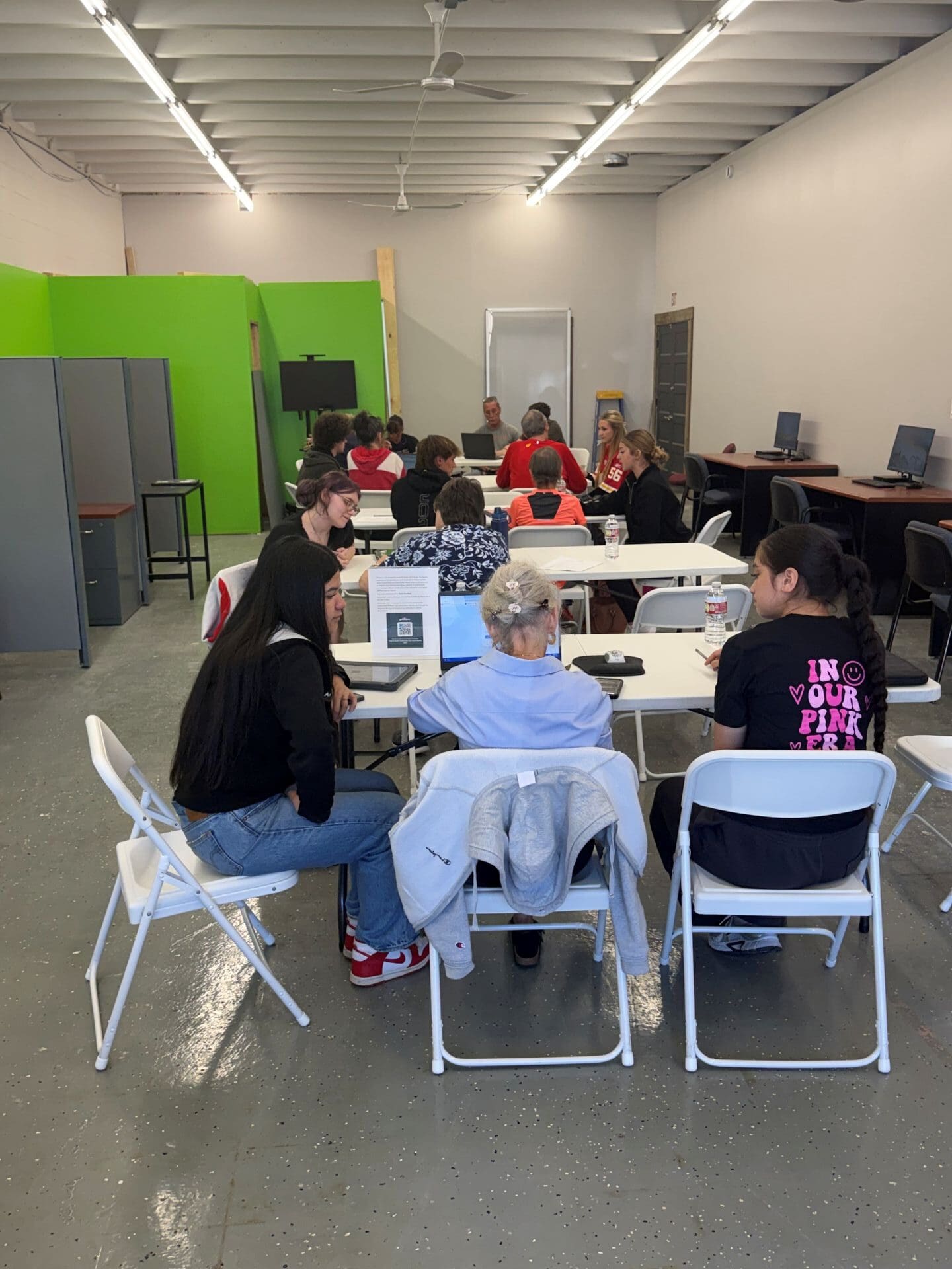 Studnets and older adults sitting at long tables looking at computers and devices together